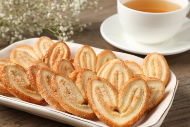 Photo of Tasty french palmier cookies, tea and gypsophila flowers on wooden table, closeup