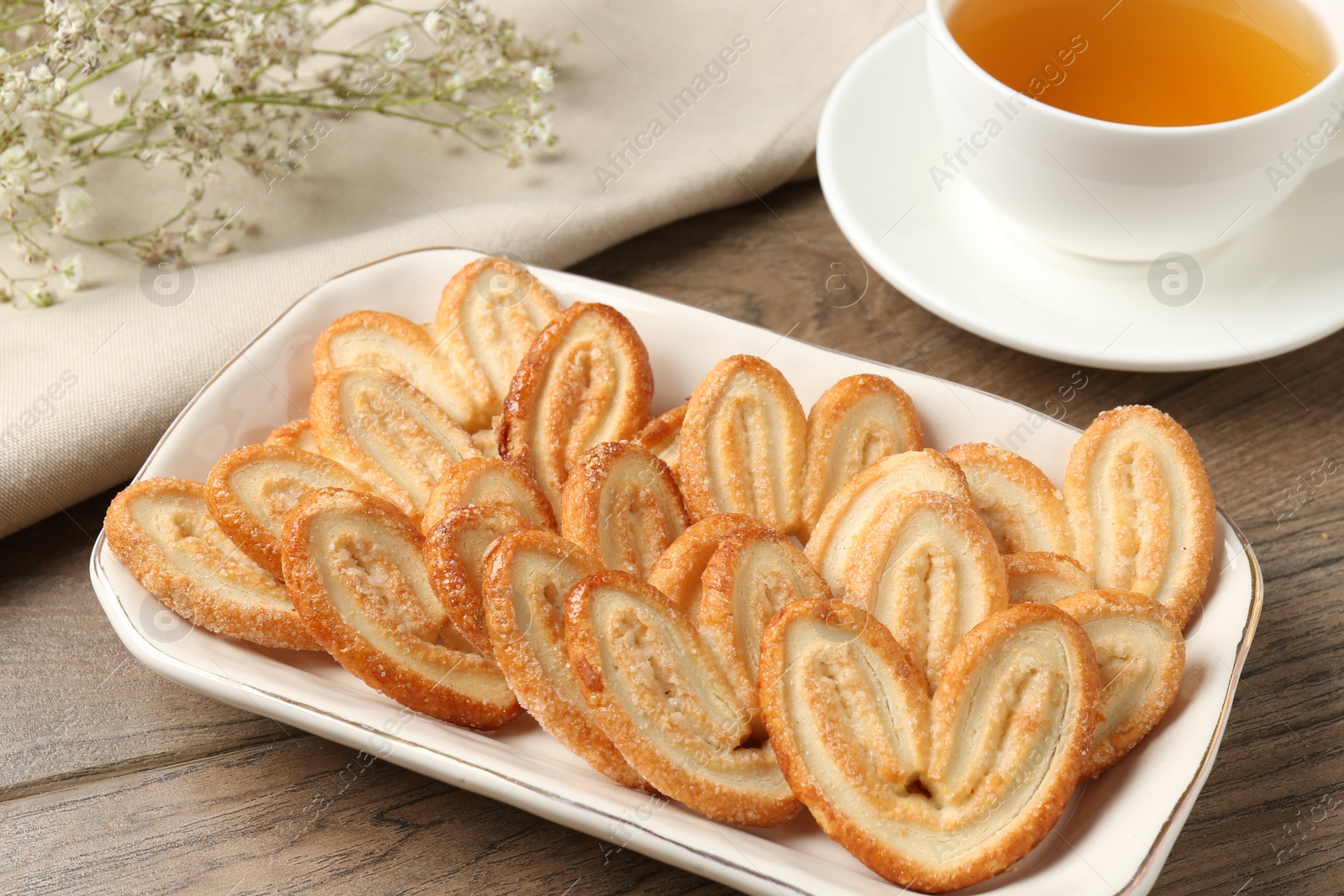 Photo of Tasty french palmier cookies, tea and gypsophila flowers on wooden table, closeup