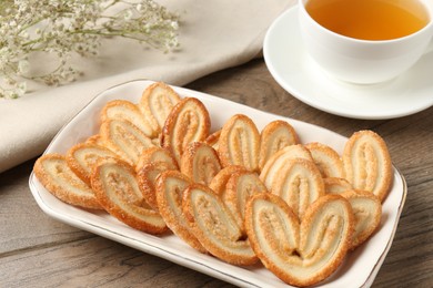 Photo of Tasty french palmier cookies, tea and gypsophila flowers on wooden table, closeup