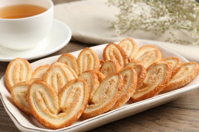 Photo of Tasty french palmier cookies, tea and gypsophila flowers on wooden table, closeup