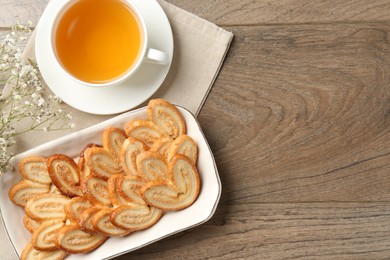 Photo of Tasty french palmier cookies, tea and gypsophila flowers on wooden table, flat lay. Space for text