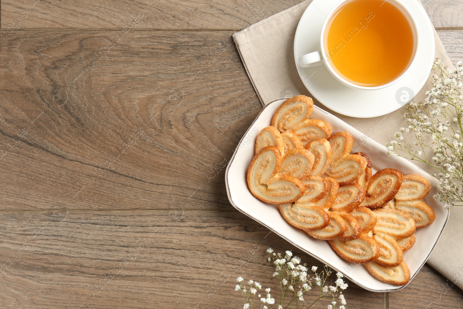 Photo of Tasty french palmier cookies, tea and gypsophila flowers on wooden table, flat lay. Space for text