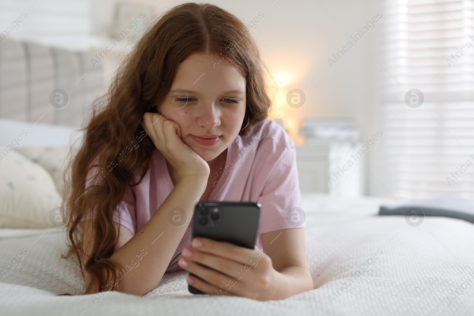 Photo of Beautiful teenage girl using smartphone on bed at home