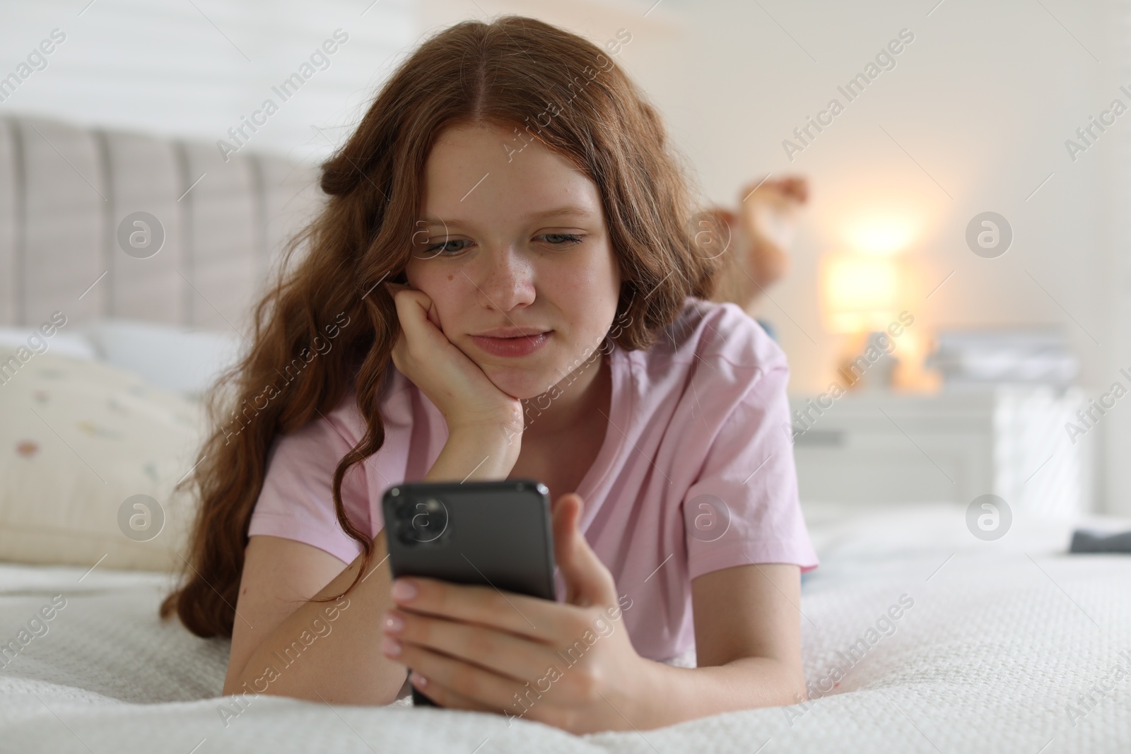 Photo of Beautiful teenage girl using smartphone on bed at home