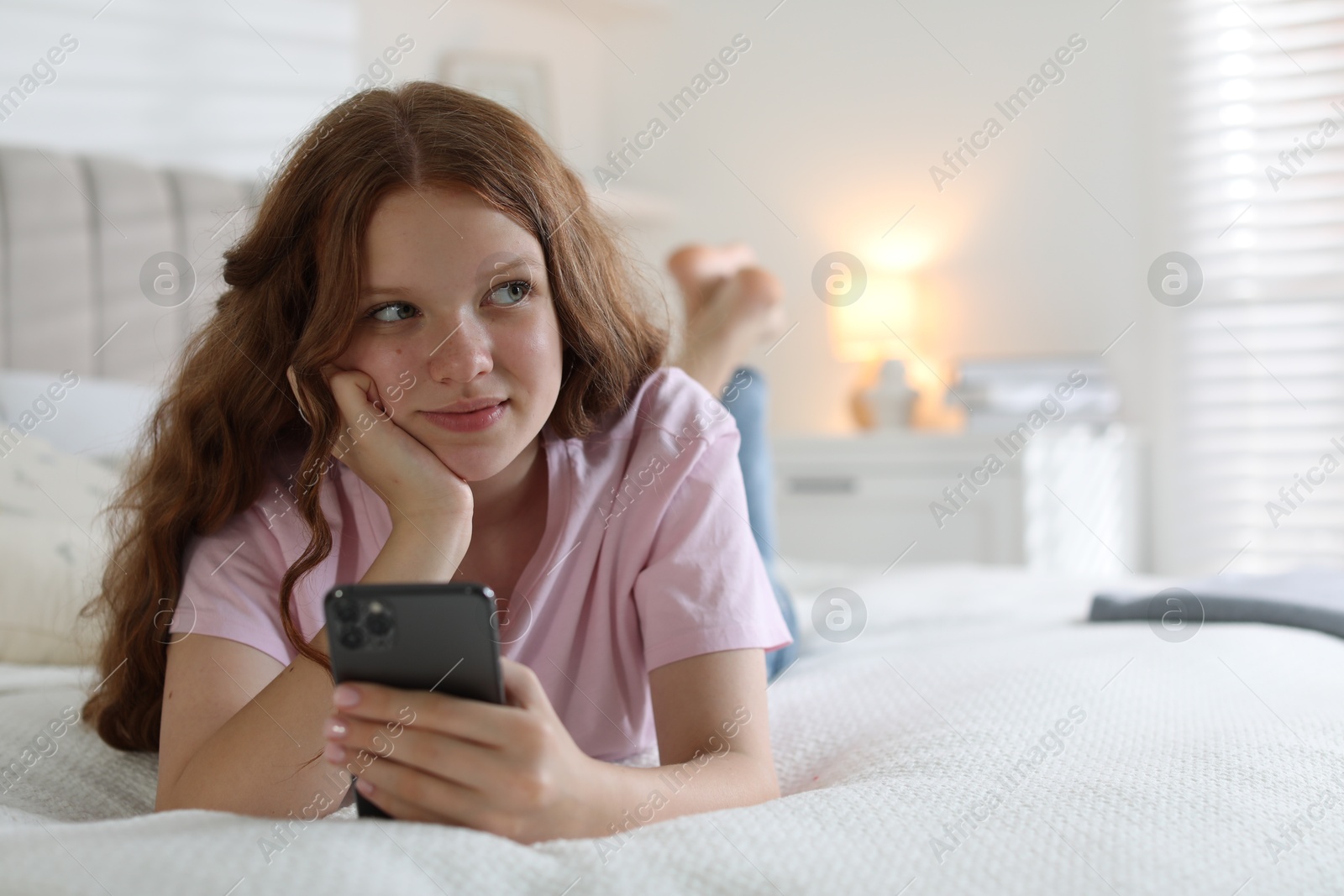 Photo of Beautiful teenage girl using smartphone on bed at home, space for text