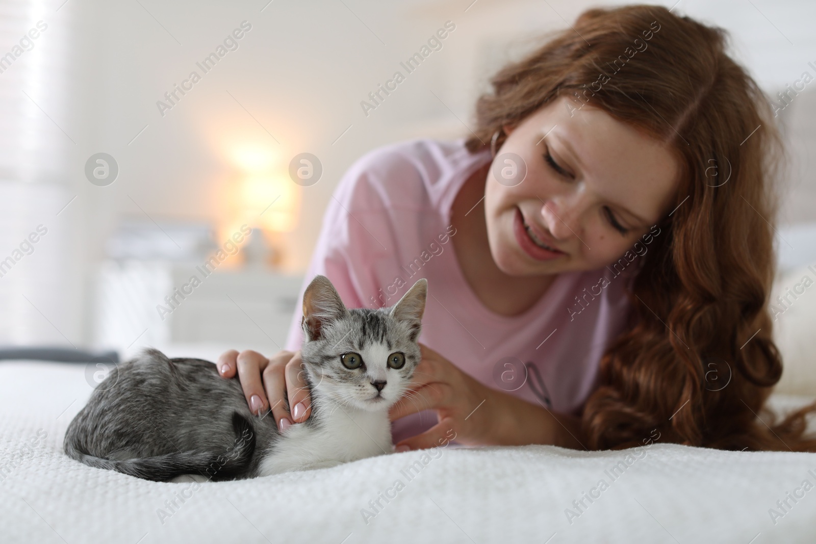 Photo of Beautiful teenage girl with cute cat on bed at home, selective focus