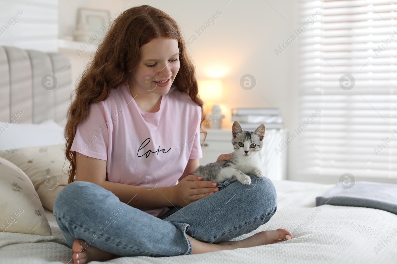 Photo of Beautiful teenage girl with cute cat on bed at home