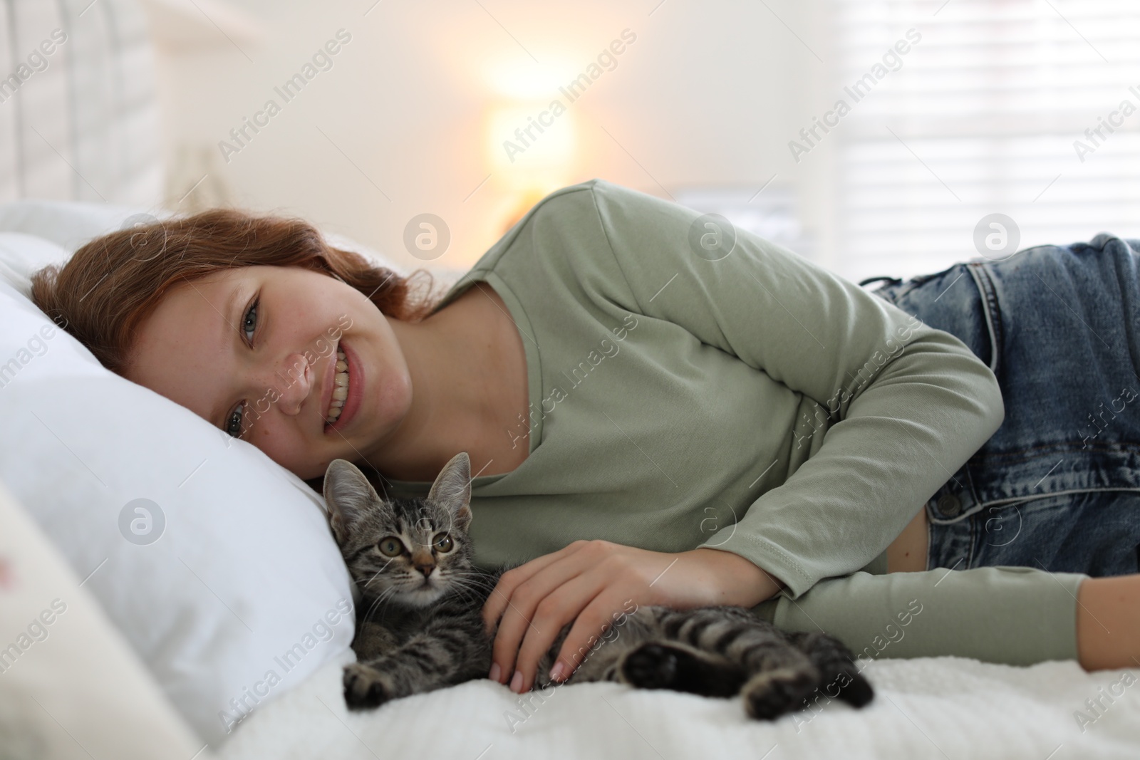 Photo of Beautiful teenage girl with cute cat on bed at home