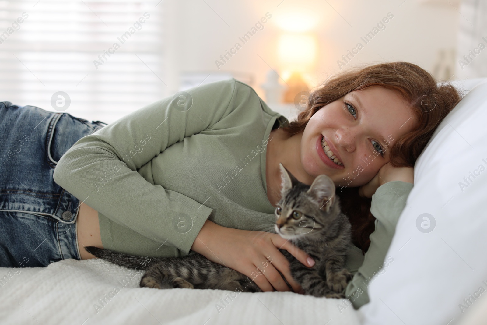 Photo of Beautiful teenage girl with cute cat on bed at home