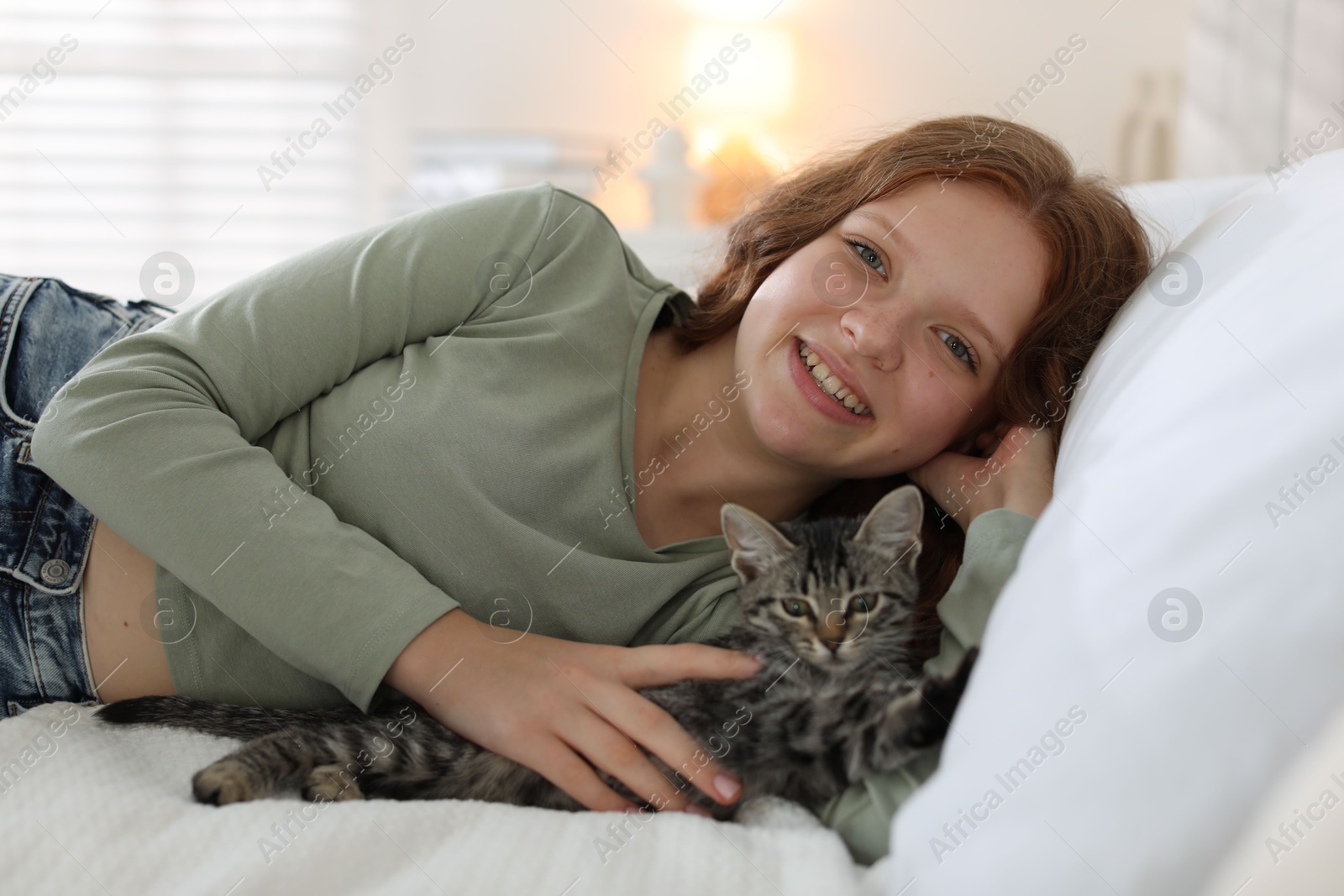 Photo of Beautiful teenage girl with cute cat on bed at home