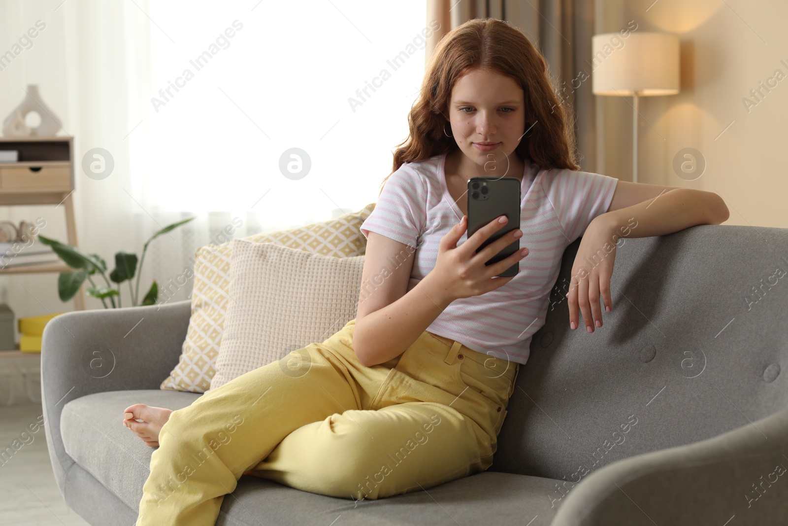 Photo of Beautiful teenage girl using smartphone on sofa at home