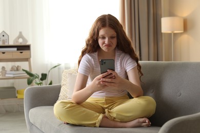 Beautiful teenage girl using smartphone on sofa at home