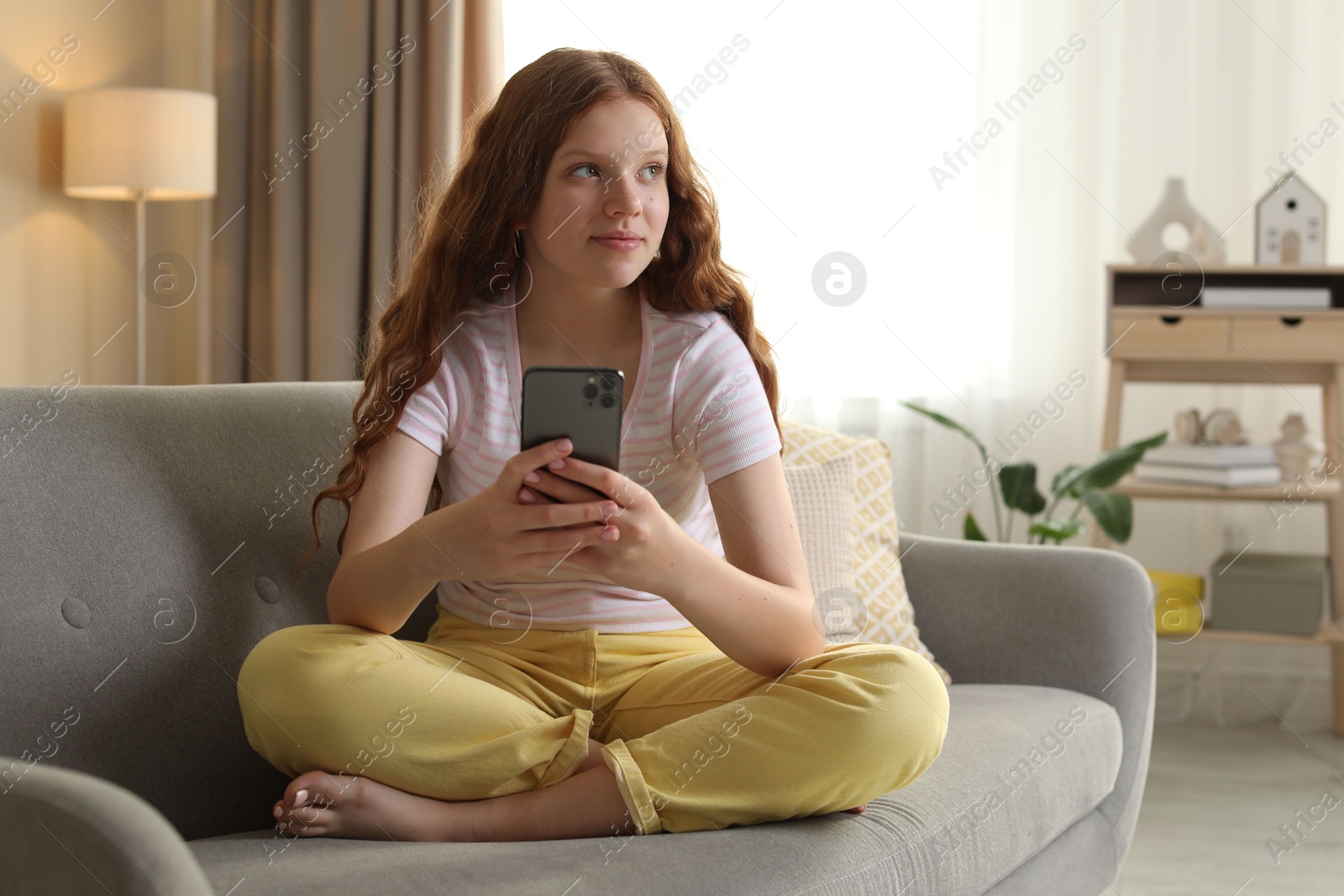 Photo of Beautiful teenage girl using smartphone on sofa at home