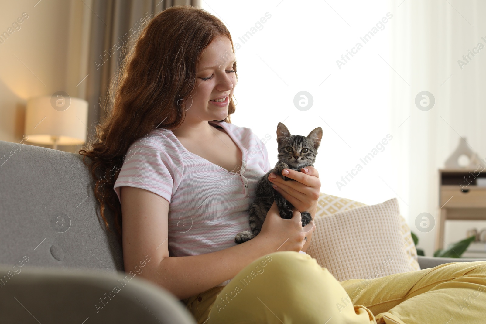 Photo of Beautiful teenage girl with cute cat on sofa at home