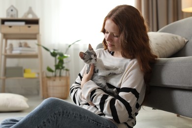 Beautiful teenage girl with cute cat on floor at home