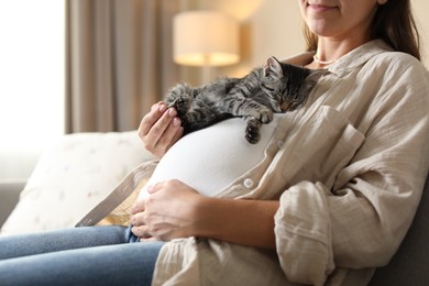 Photo of Pregnant woman with cute cat sleeping on her belly at home, closeup