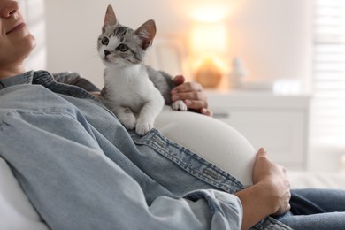 Photo of Pregnant woman with cute cat on her belly at home, closeup