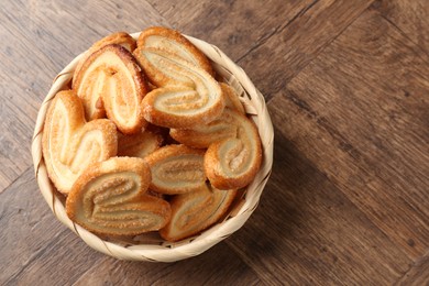 Photo of Tasty french palmier cookies in wicker bowl on wooden table, top view. Space for text