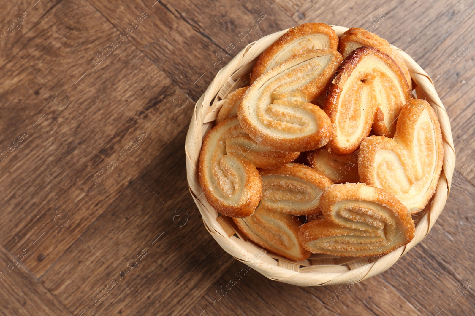 Photo of Tasty french palmier cookies in wicker bowl on wooden table, top view. Space for text