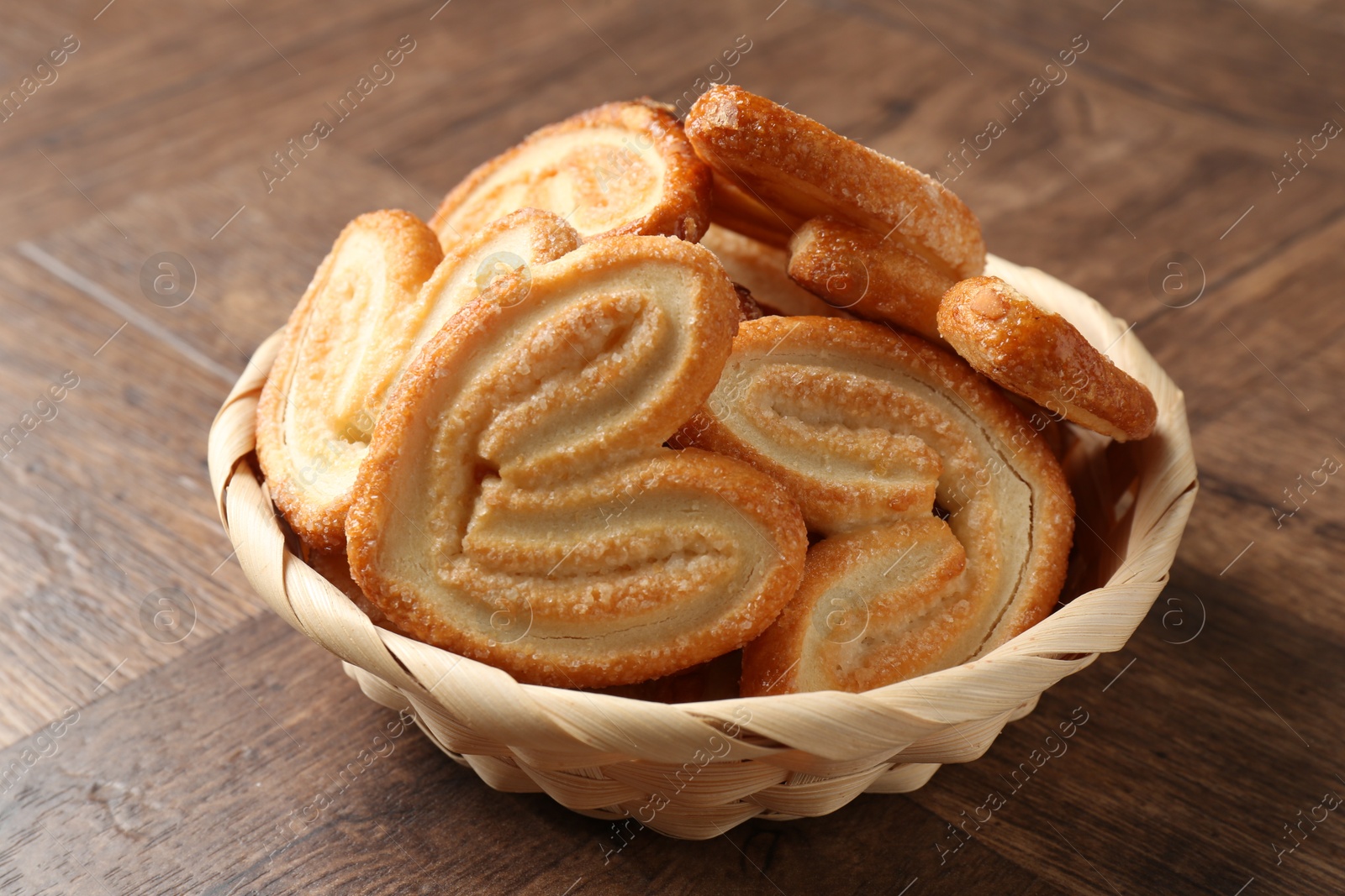 Photo of Tasty french palmier cookies in wicker bowl on wooden table, closeup