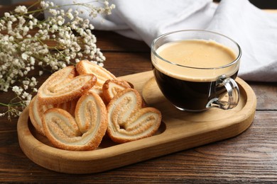 Photo of Tasty french palmier cookies, coffee and gypsophila flowers on wooden table, closeup