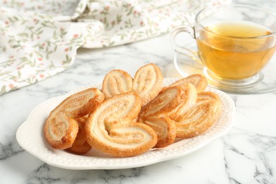 Photo of Delicious palmier cookies with tea on white marble table, closeup