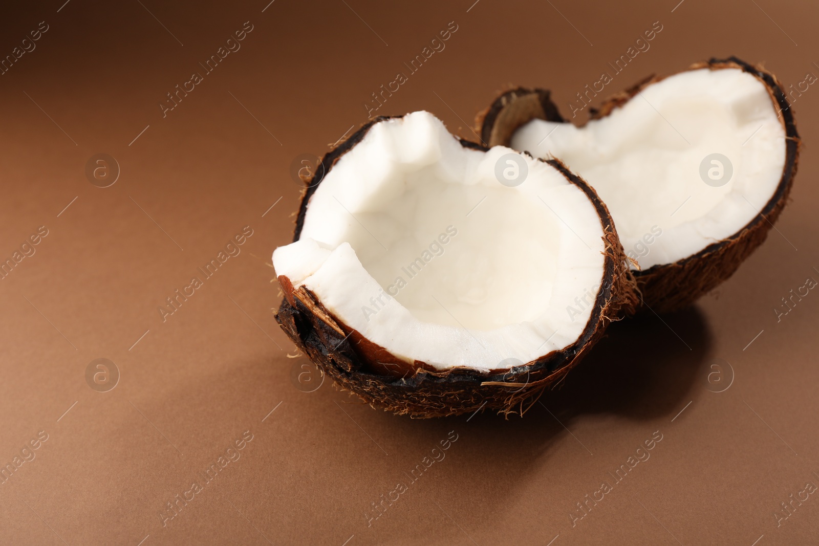 Photo of Halves of cracked coconut on brown background, closeup. Space for text