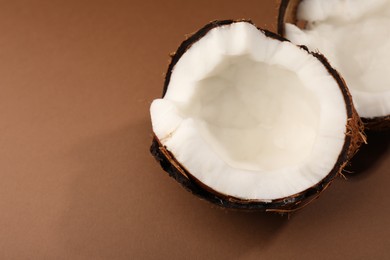 Photo of Halves of cracked coconut on brown background, closeup. Space for text