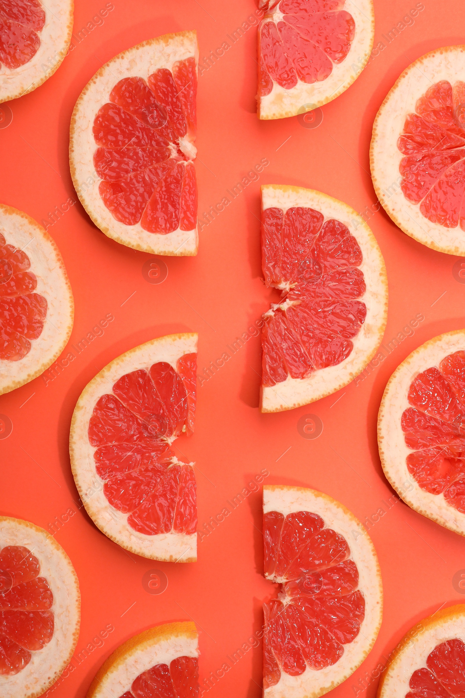 Photo of Slices of grapefruit in coral color background, flat lay