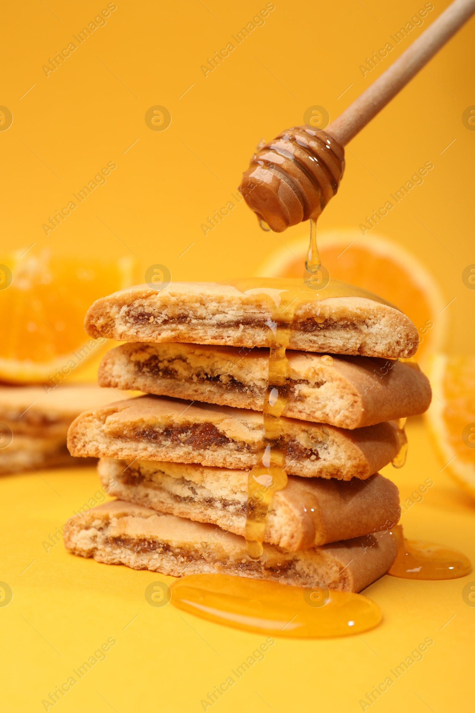 Photo of Pouring honey onto cookies on orange background, closeup