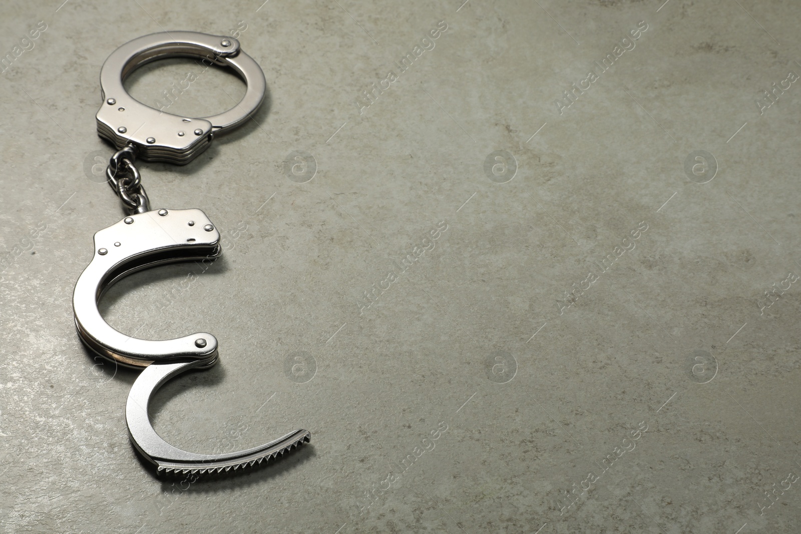 Photo of Classic chain handcuffs on grey table, space for text