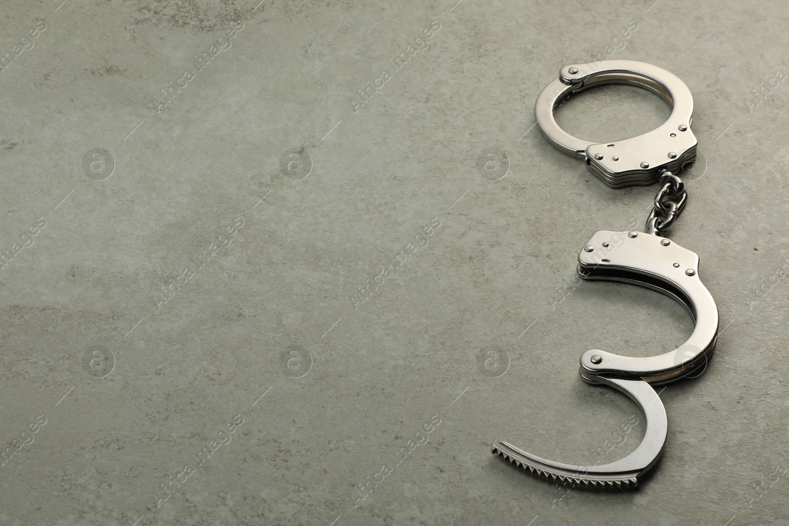 Photo of Classic chain handcuffs on grey table, space for text