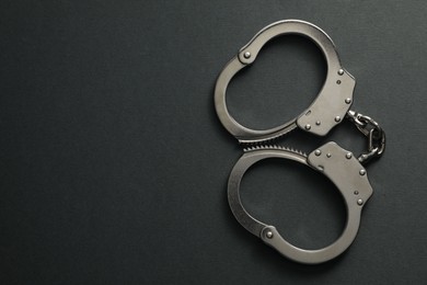 Photo of Classic chain handcuffs on black background, top view. Space for text