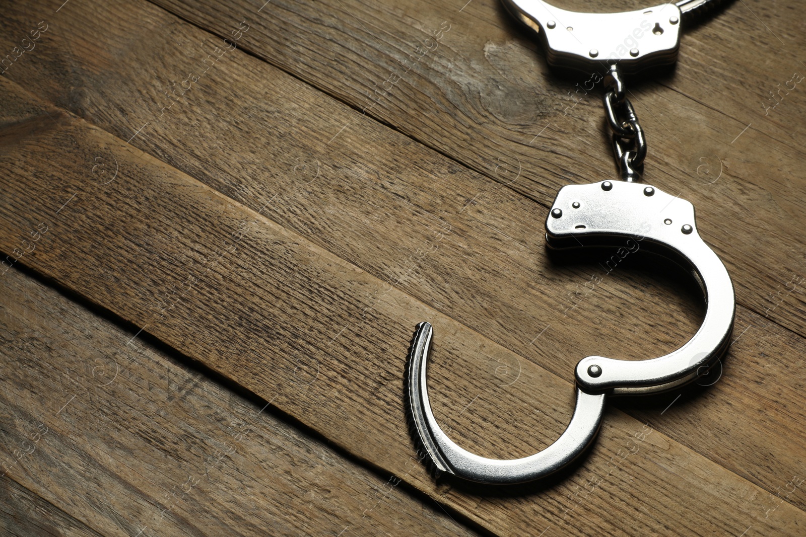 Photo of Classic chain handcuffs on wooden table, closeup. Space for text