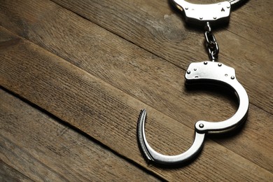 Classic chain handcuffs on wooden table, closeup. Space for text