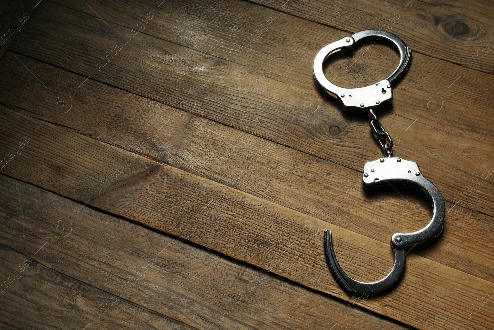 Photo of Classic chain handcuffs on wooden table, top view. Space for text