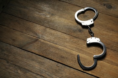 Photo of Classic chain handcuffs on wooden table, top view. Space for text