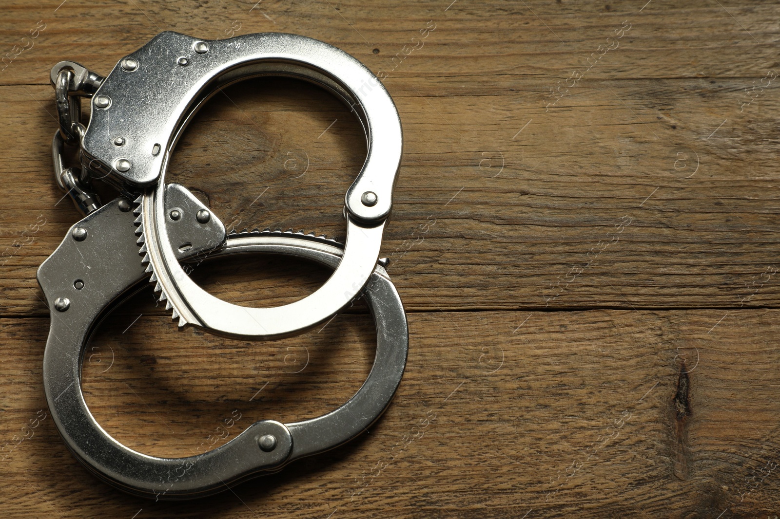 Photo of Classic chain handcuffs on wooden table, top view. Space for text