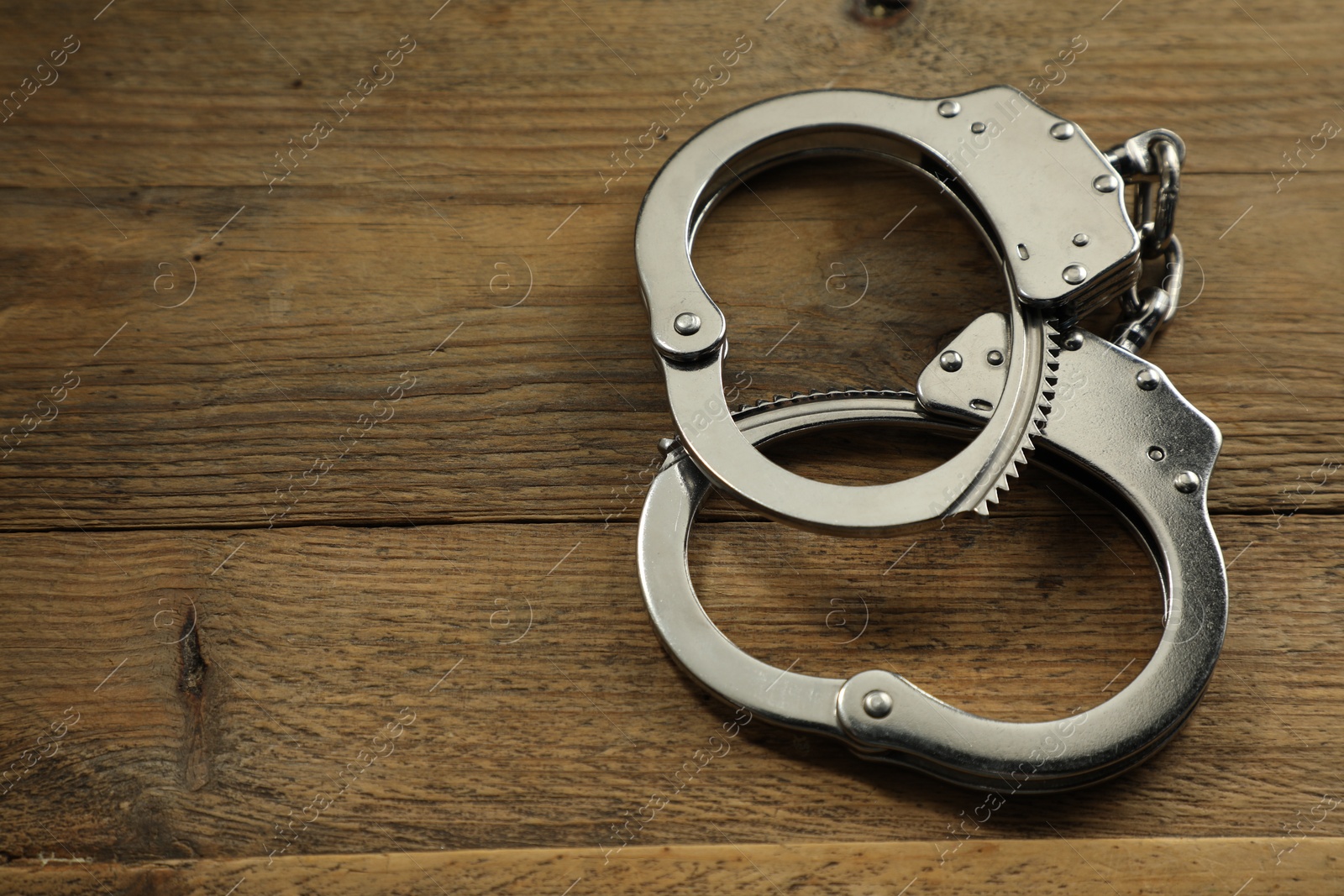 Photo of Classic chain handcuffs on wooden table, closeup. Space for text