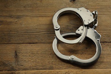 Photo of Classic chain handcuffs on wooden table, closeup. Space for text