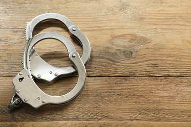 Photo of Classic chain handcuffs on wooden table, closeup. Space for text