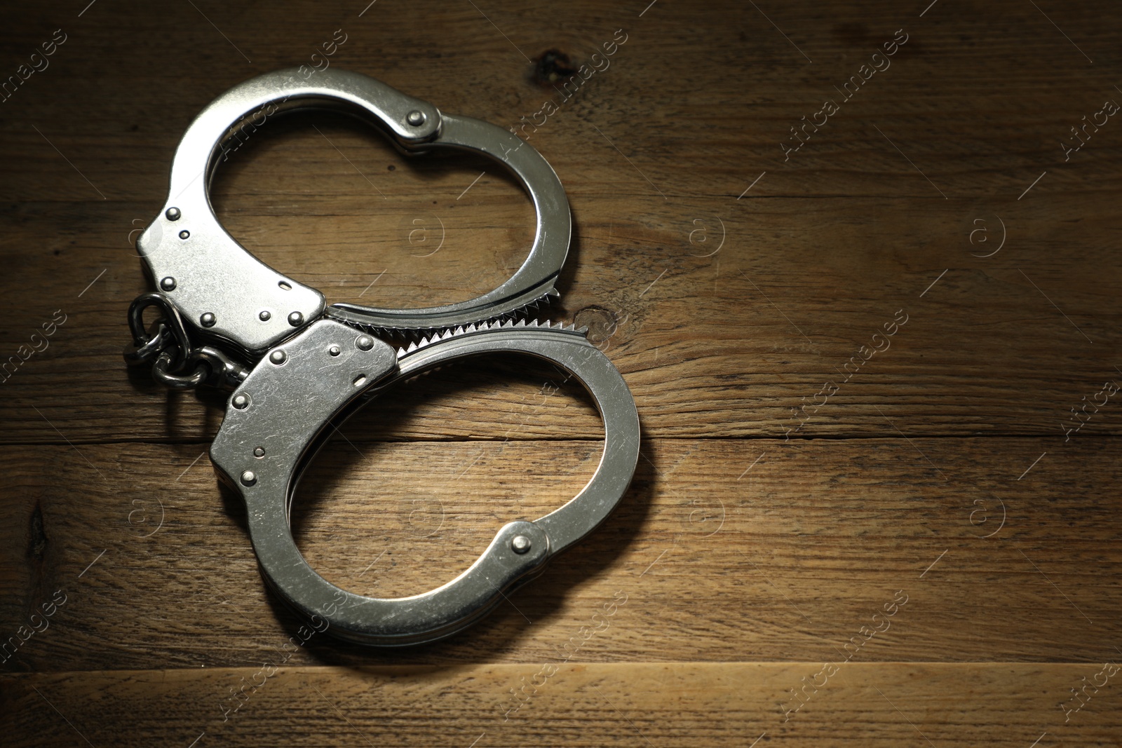 Photo of Classic chain handcuffs on wooden table, closeup. Space for text