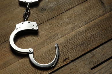 Photo of Classic chain handcuffs on wooden table, closeup. Space for text