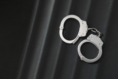 Photo of Classic chain handcuffs on black table, top view. Space for text