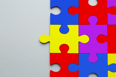 Many colorful puzzle pieces on light grey background, top view. Symbol of autism