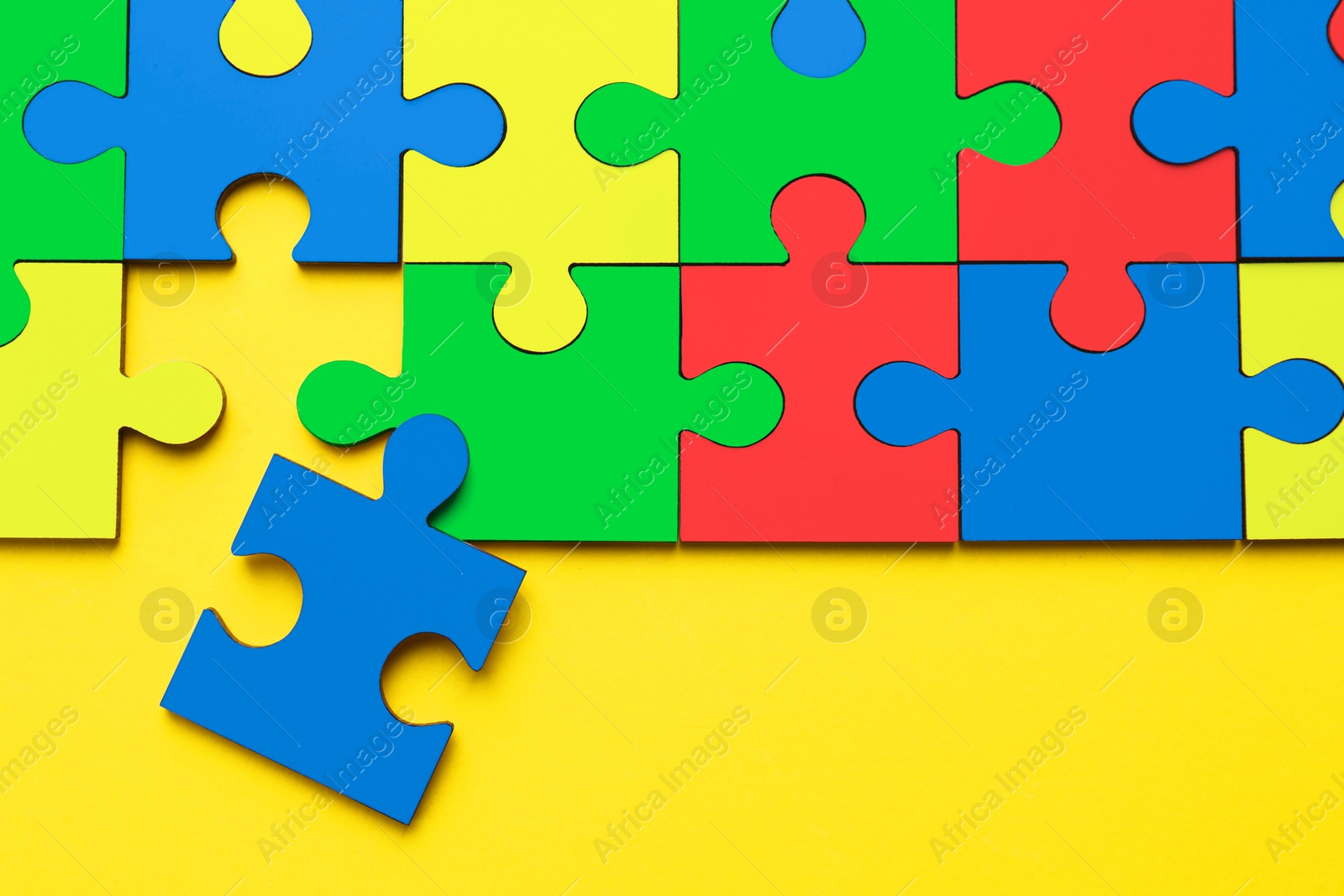 Image of Many colorful puzzle pieces on yellow background, top view. Symbol of autism