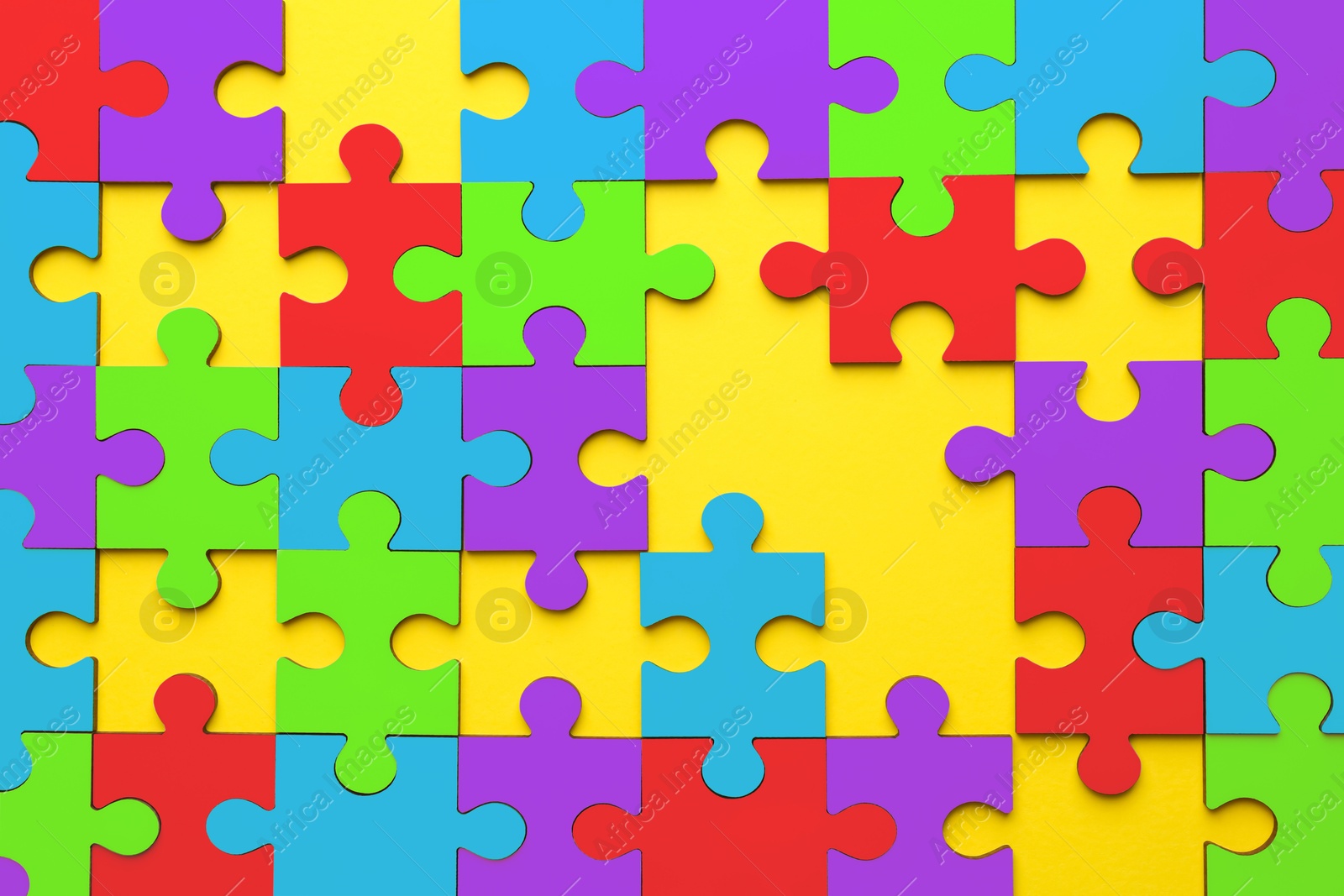 Image of Many colorful puzzle pieces on yellow background, top view. Symbol of autism