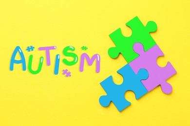 Image of Autism word and colorful puzzle pieces on yellow background, top view