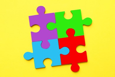 Image of Four colorful puzzle pieces on yellow background, top view. Symbol of autism