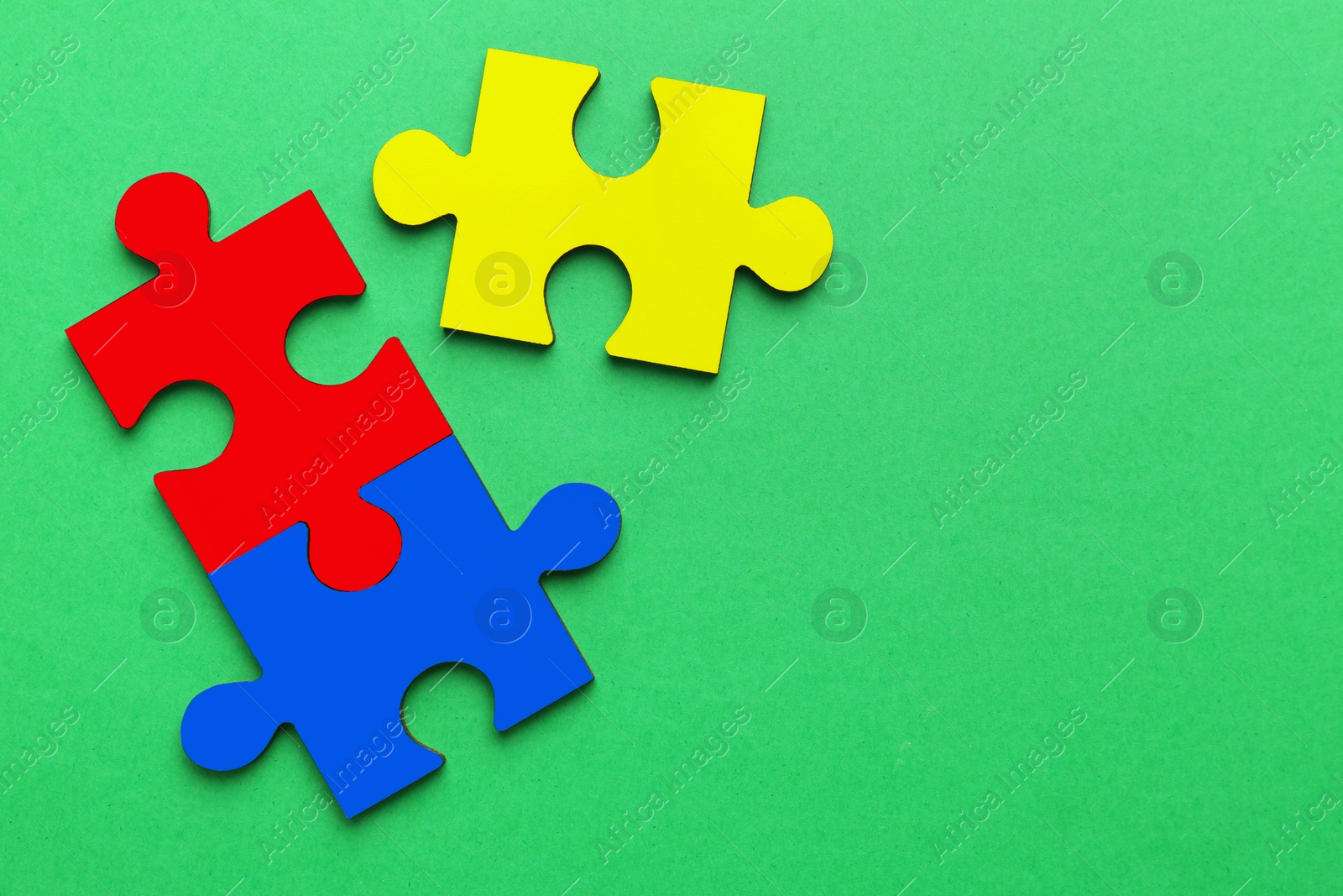 Image of Three colorful puzzle pieces on green background, top view. Symbol of autism